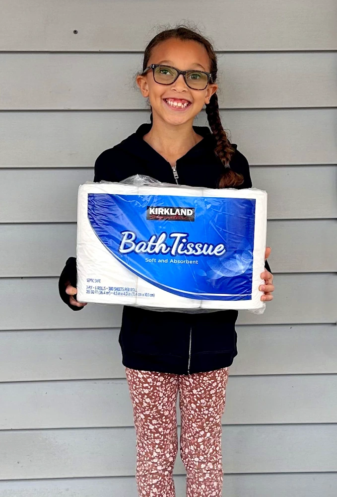 A smiling girl holds a donation of paper towels.